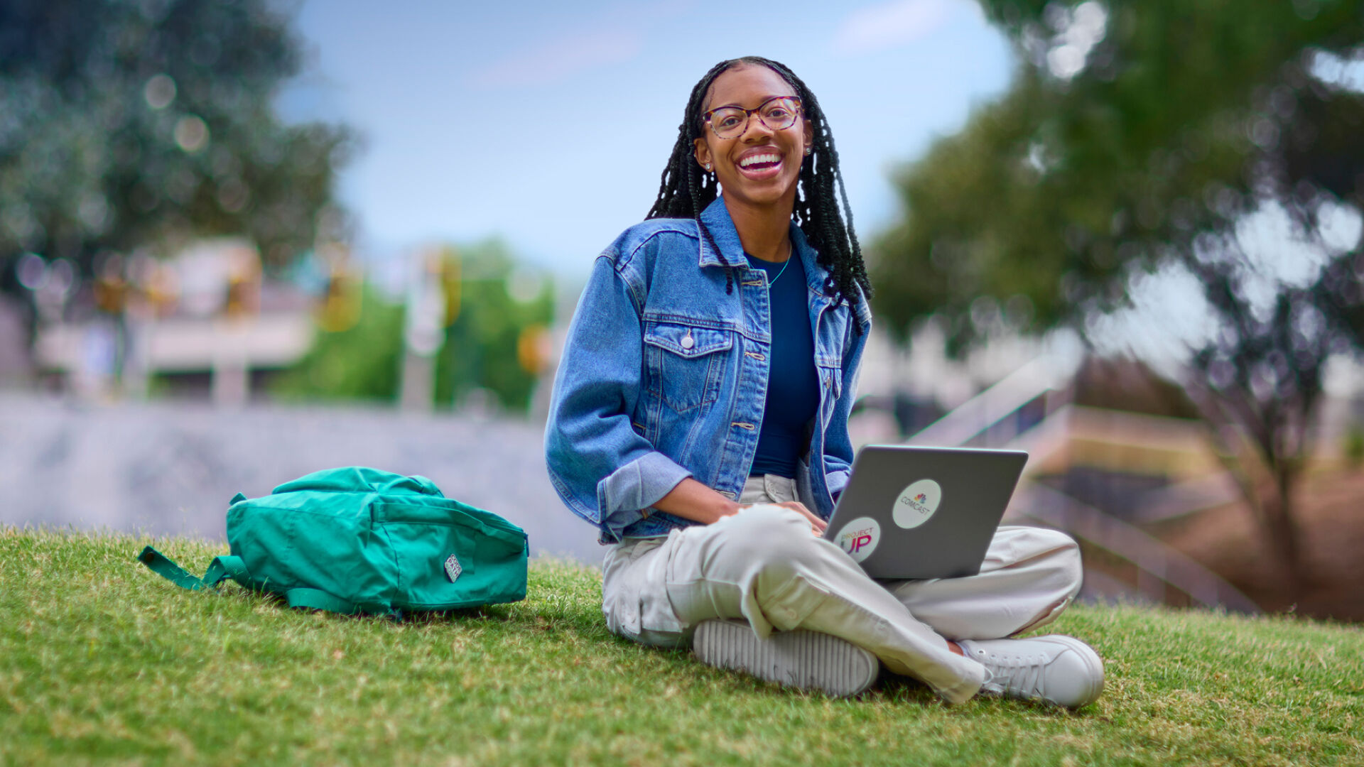 A woman using a laptop while sitting in a field of grass.