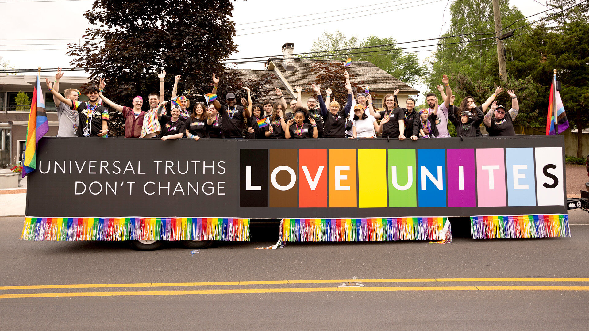 Pride parade participants holding up a 'Love Unites' banner.