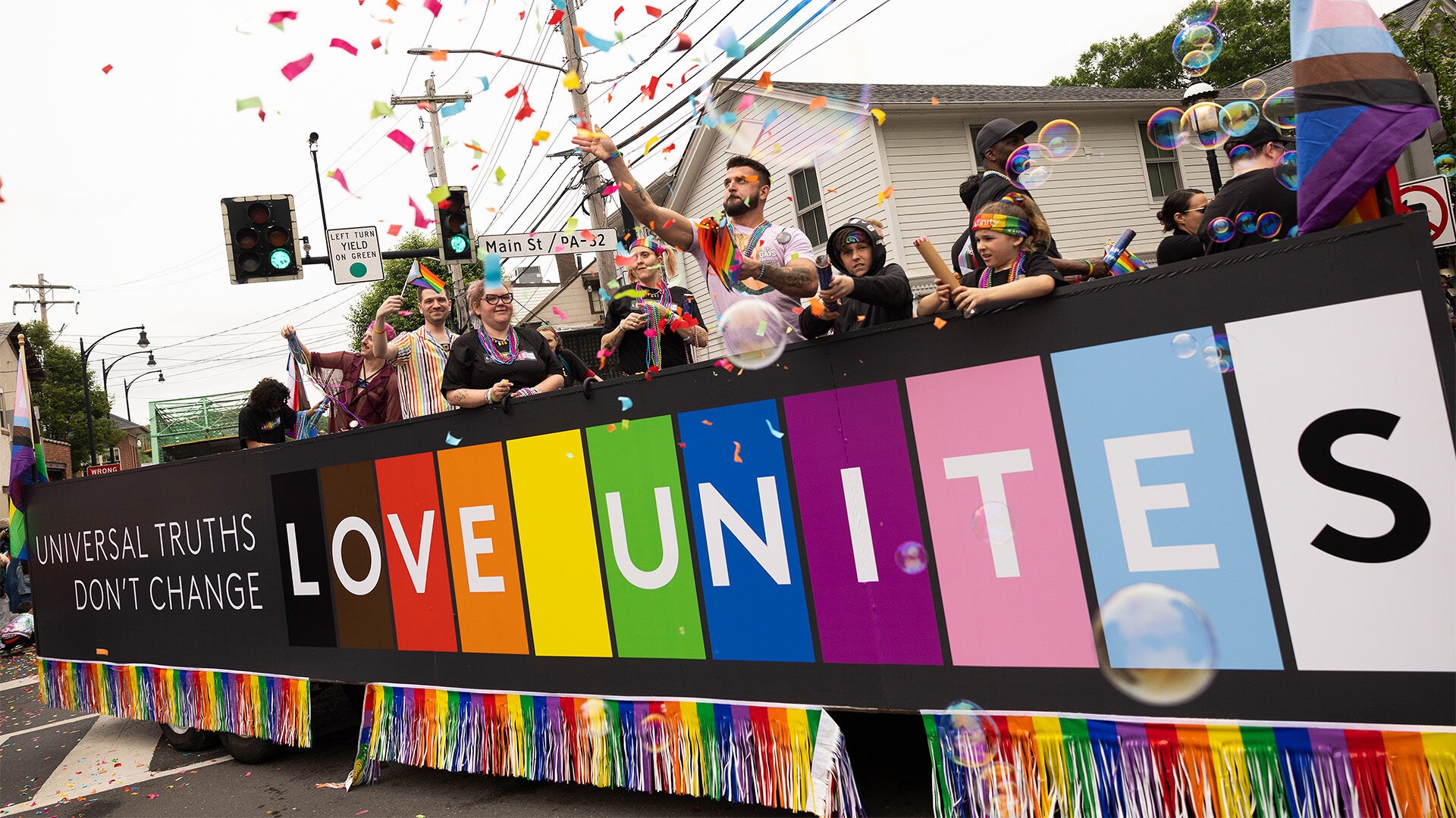 Pride parade participants holding up a 'Love Unites' banner.