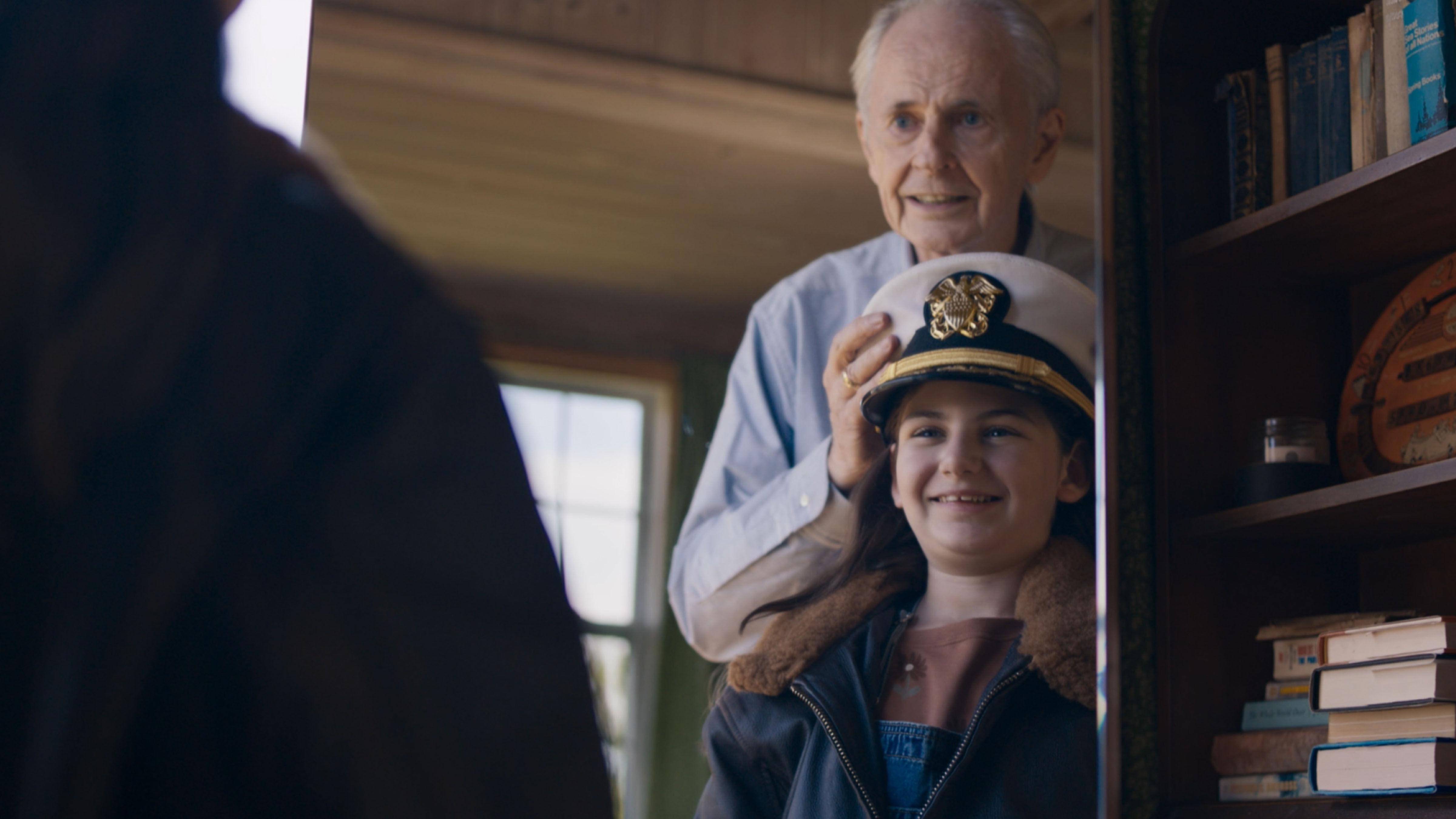 An elderly man with his granddaughter, looking in the mirror. The granddaughter is wearing her grandfather's old Military uniform and is smiling.