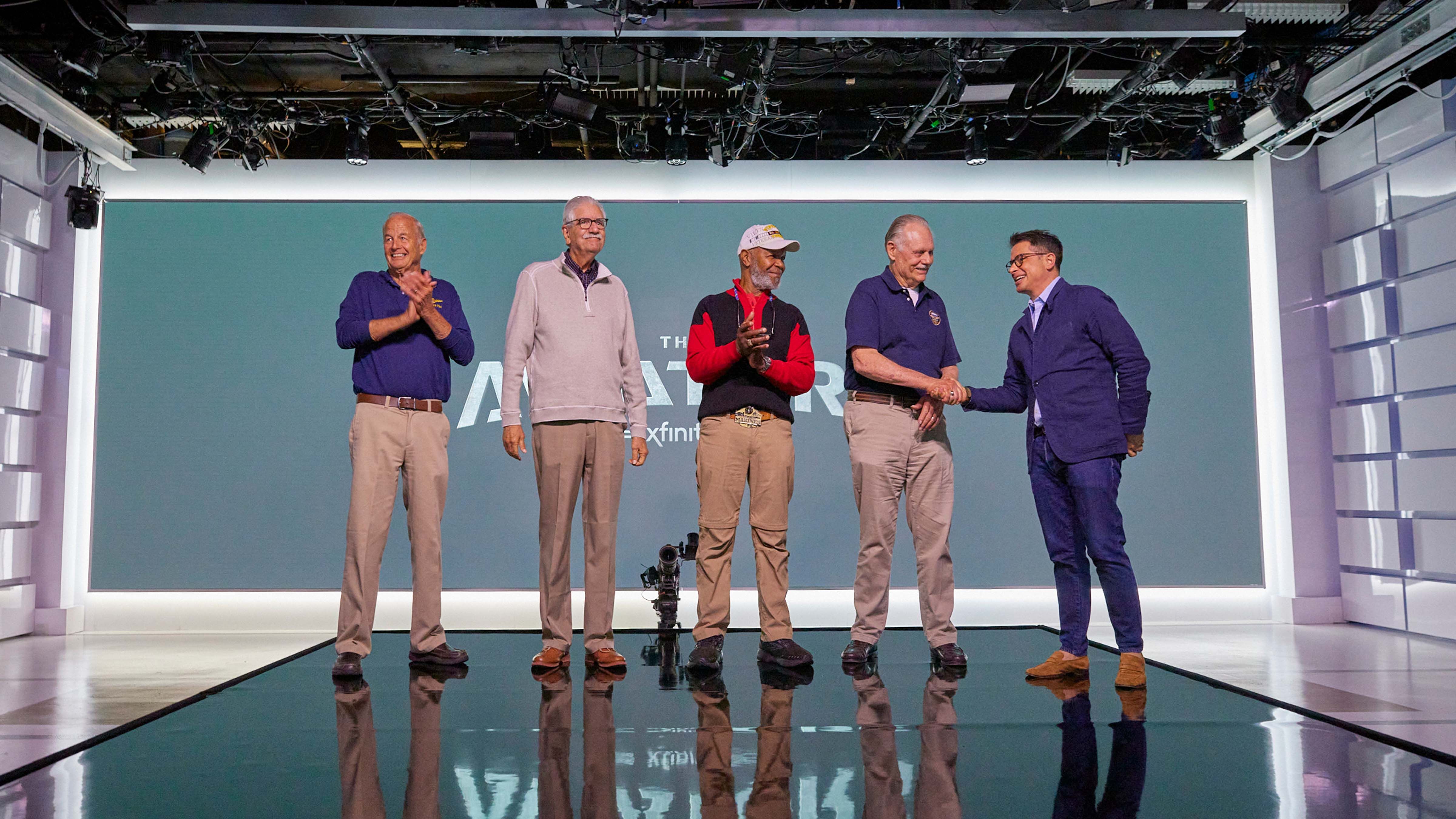 Four army veterans, James 'Zeke' Lloyd, Bill 'Offender' Moir, Elester 'Hollywood' Latham, Jack 'Razor' Gillett, standing on a stage in front of a screen.