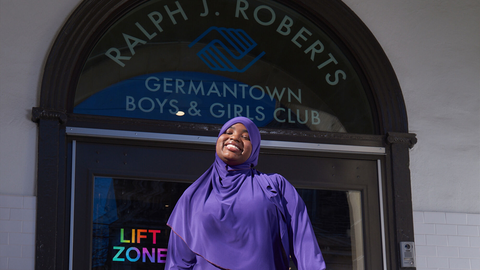 A student standing in front of the Ralph J. Roberts Germantown Boys & Girls Club.